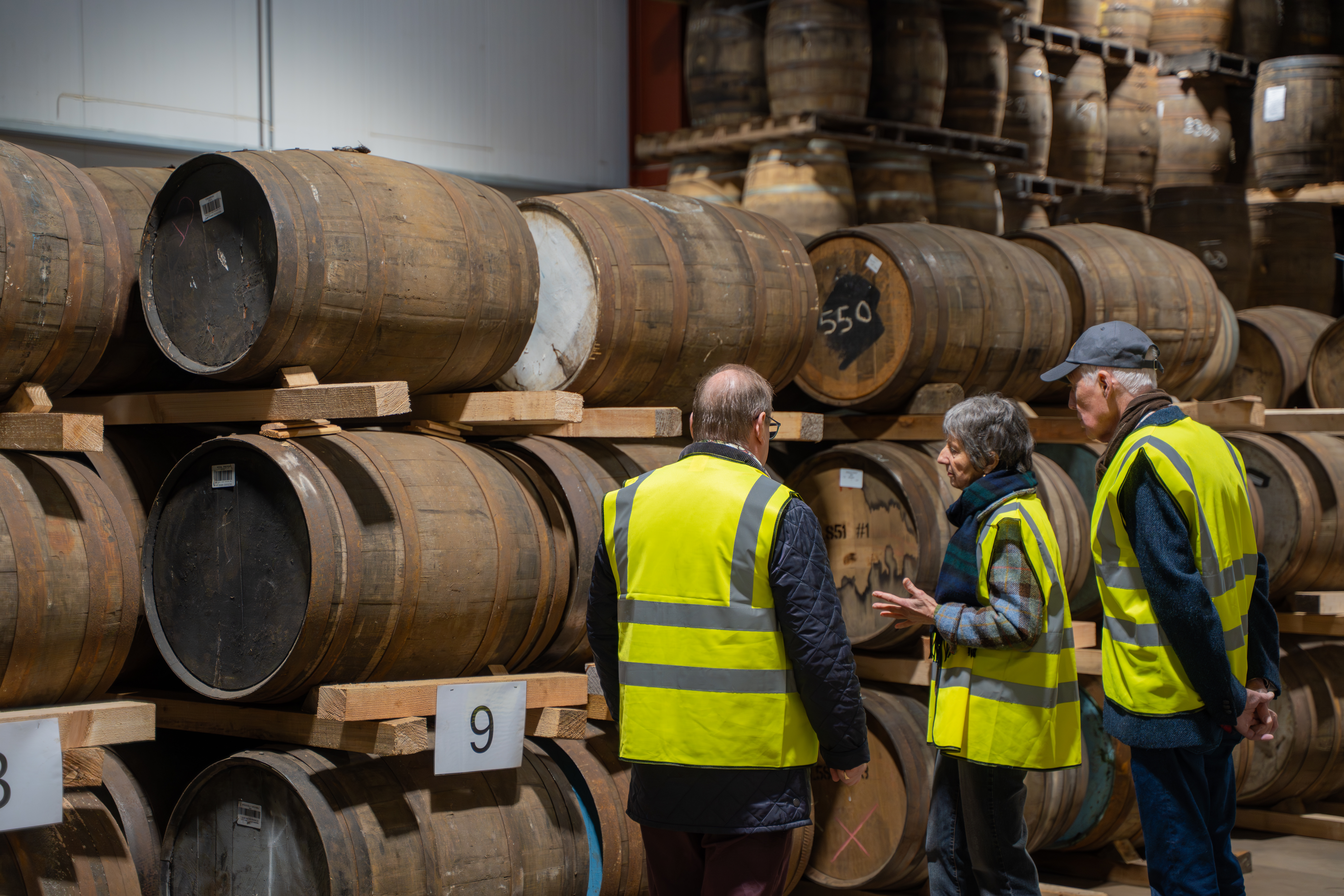 Three people wearing yellow high visability jackets walking around the Cask Trade Warehouse and looking at casks of whisky